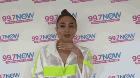 a woman is standing in front of a wall with 99.7 now written on it