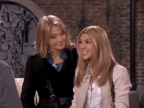 two women standing next to each other in front of a brick wall .