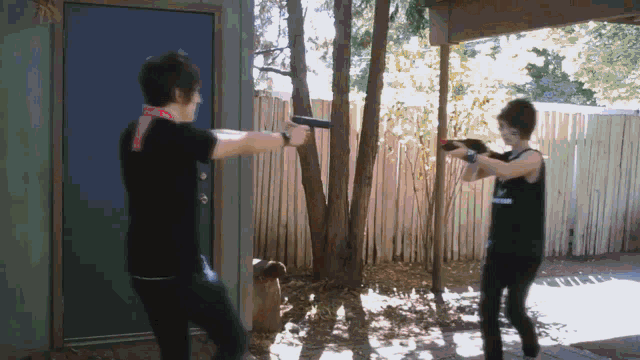 two people are standing in front of a fence and one is holding a gun and the other is holding a sword