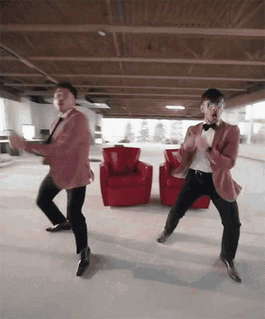 two men in suits and bow ties are dancing in a living room