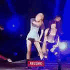 a couple of women are dancing on a stage with a record sign in the background .