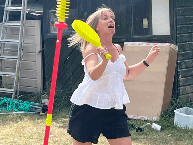 a woman in a white top and black shorts is holding a yellow badminton racquet