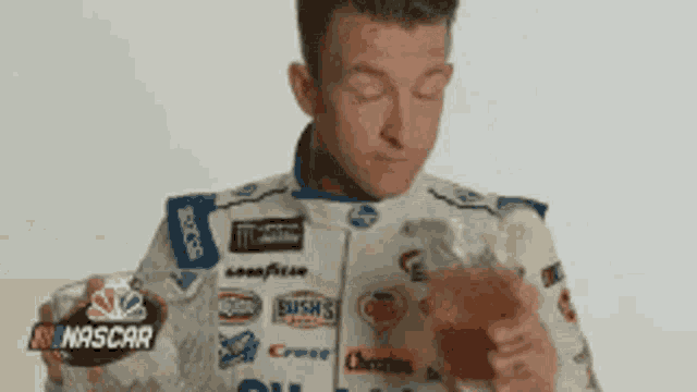 a man in a nascar jacket is eating a hot dog