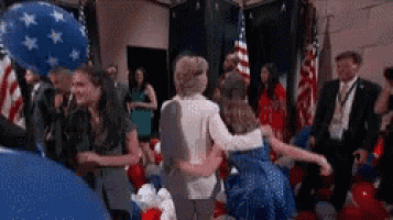 a woman is hugging another woman in a room filled with balloons and flags .