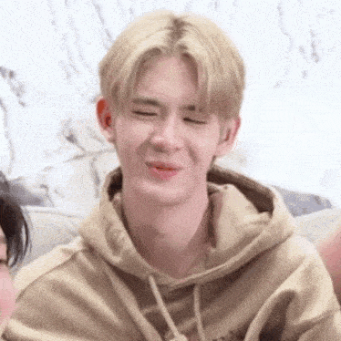 a young man in a tan hoodie is making a funny face .