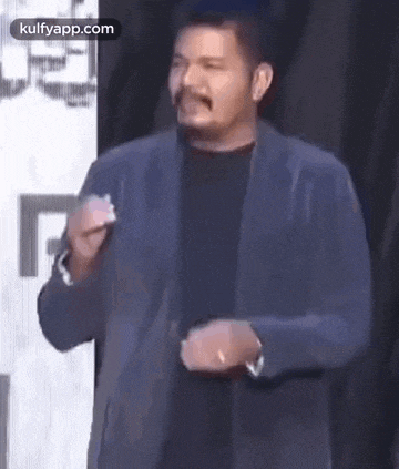 a man in a suit is giving a speech on a stage and making a funny face .