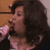 a woman is drinking from a glass with a fork in her mouth