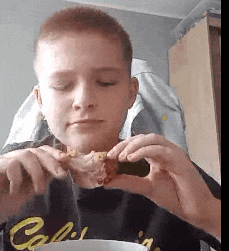 a young boy in a california shirt is eating a piece of pizza .