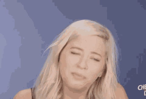 a woman with blonde hair is making a funny face in front of a blue wall .
