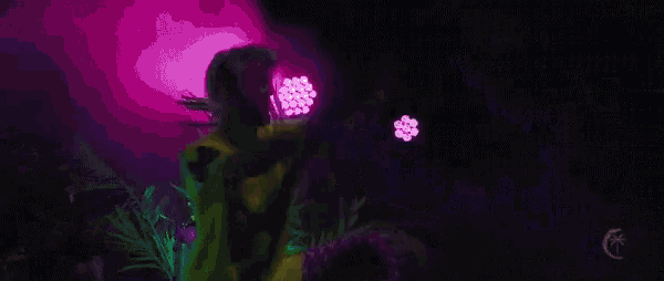 a man in a yellow shirt is dancing in a dark room with purple lights .
