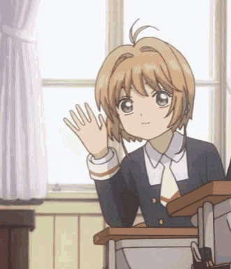 a girl in a school uniform is sitting at a desk waving her hand in a classroom .