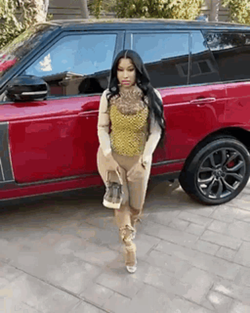 a woman is standing in front of a red car holding a purse .