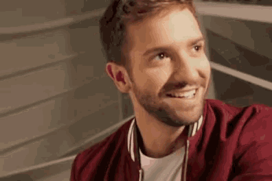 a man with a beard wearing a red jacket and a white shirt smiles