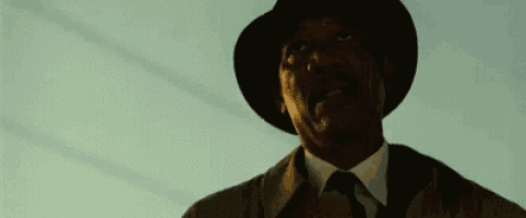 a man in a suit and tie is wearing a hat and looking up at the sky .