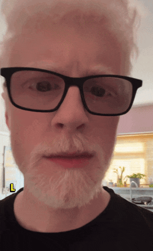 a man with glasses and a beard has a yellow l sticker on his face