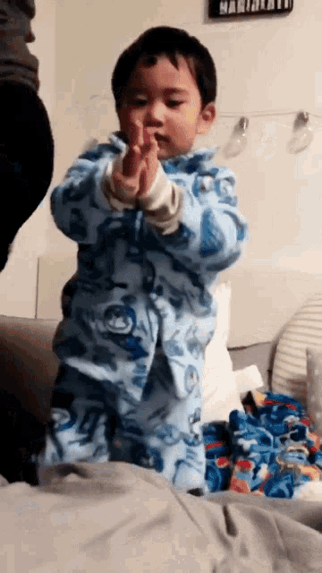a little boy wearing a blue pajama set is standing on a bed