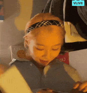 a girl wearing a plaid headband is looking at her phone with a vlive logo in the background
