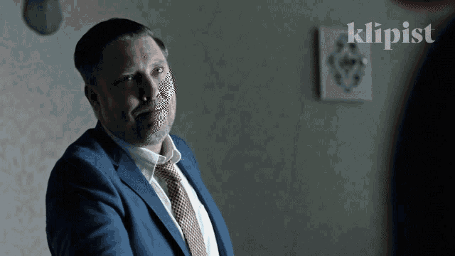 a man in a suit and tie is standing in front of a wall with the word klipist on it