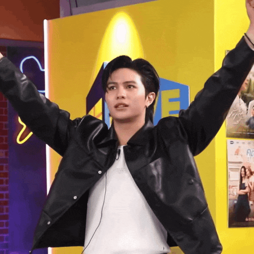 a man in a black jacket is standing with his arms outstretched in front of a sign that says ' a '