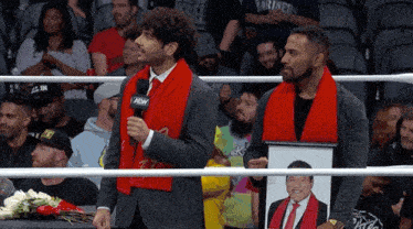 two men in a wrestling ring holding a picture of a man and flowers