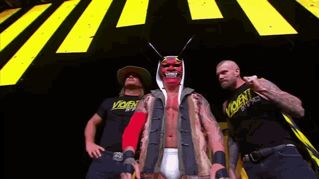 a man in a red mask is standing next to two men wearing violent shirts