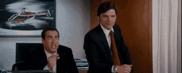 two men in suits and ties are standing in a room .