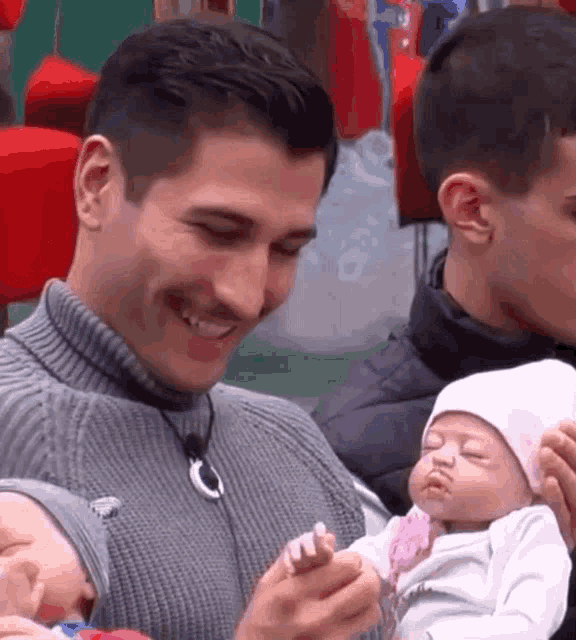 a man is holding a baby doll in his arms while another man looks on .
