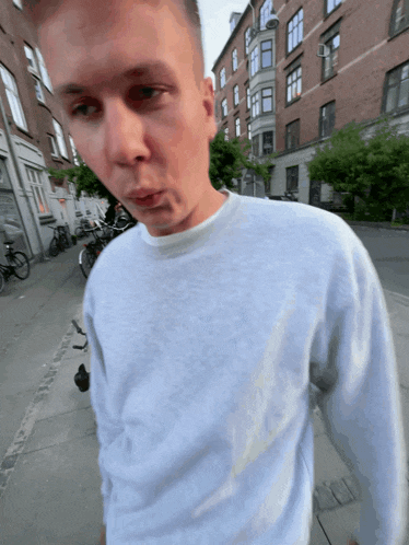 a young man wearing a grey sweater is walking down a street