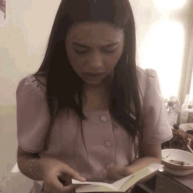 a woman in a pink shirt is looking at a book