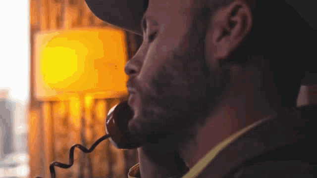 a man with a beard is talking on a telephone while wearing a hat .