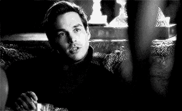 a man is sitting on a couch holding a glass of whiskey and smoking a cigarette .