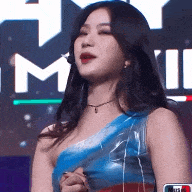 a woman wearing a blue one shoulder top is standing in front of a sign that says music .