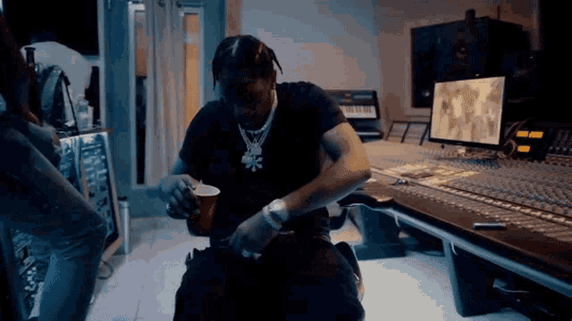 a man in a black shirt is sitting at a desk in a recording studio holding a cup of coffee .