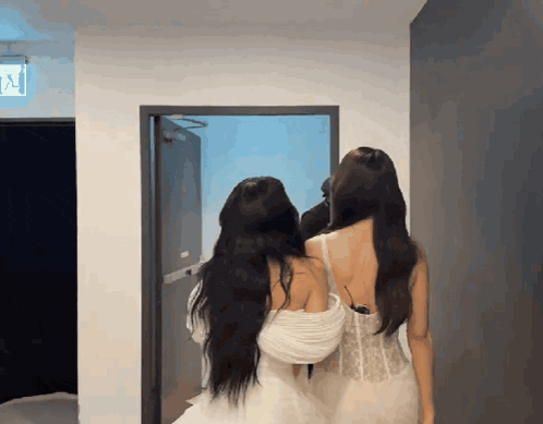 two women standing next to each other in a hallway with an exit sign on the wall