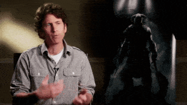 a man in a plaid shirt is talking in front of a painting