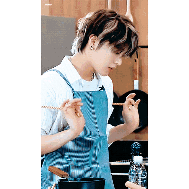a young man wearing an apron is cooking in a kitchen with a bottle of water in the background