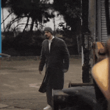a man with a beard wearing a beanie and a coat is walking down a street