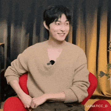 a man wearing a tan sweater is sitting in a red chair and smiling .