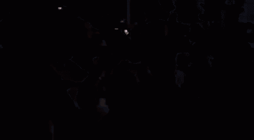 a group of men are dancing in a dark room and one of them is wearing a white shirt with the letter n on it .