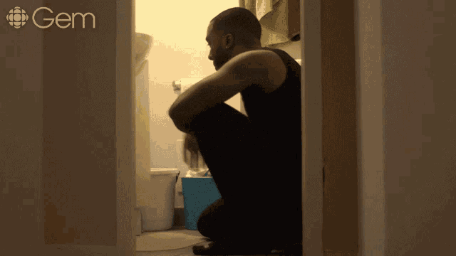 a man squatting down in a bathroom with a gem logo on the wall