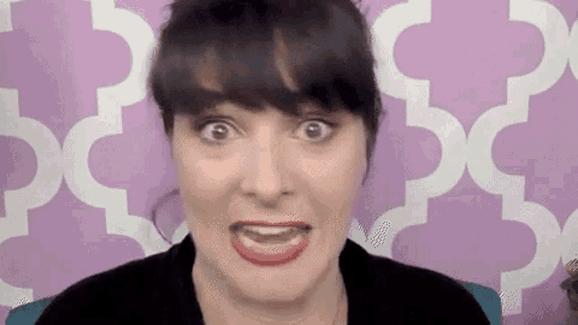 a woman with black hair and red lipstick is making a funny face in front of a purple wall .