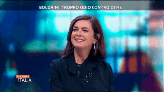 a woman is smiling in front of a screen that says ' boldrini troppo odio contro di me ' on it