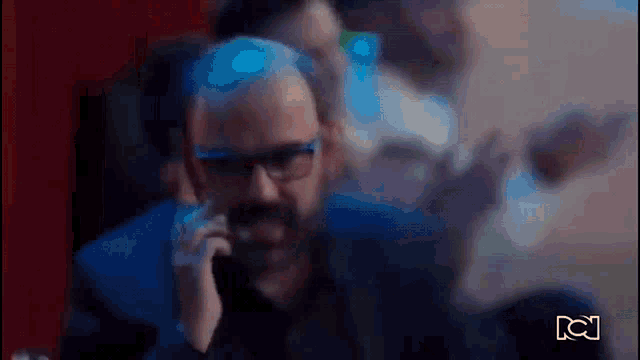 a man with a beard and glasses is talking on a cell phone .