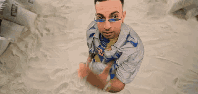 a man wearing sunglasses and a shirt that says ' lg ' on it sits in a pile of sand