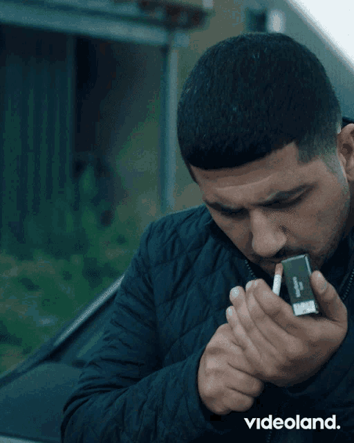 a man in a black jacket lighting a cigarette with a videoland logo in the corner