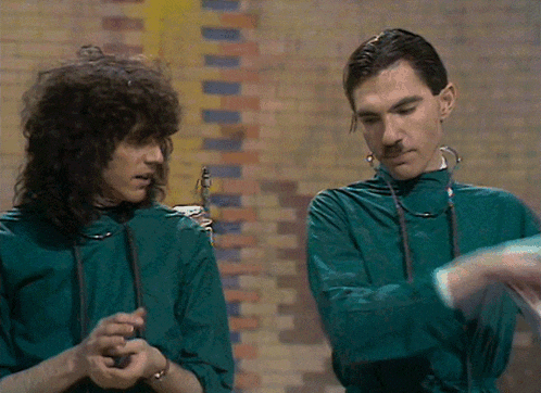 two men standing next to each other wearing green jumpsuits