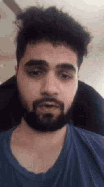 a man with a beard and a blue shirt is looking at the camera .