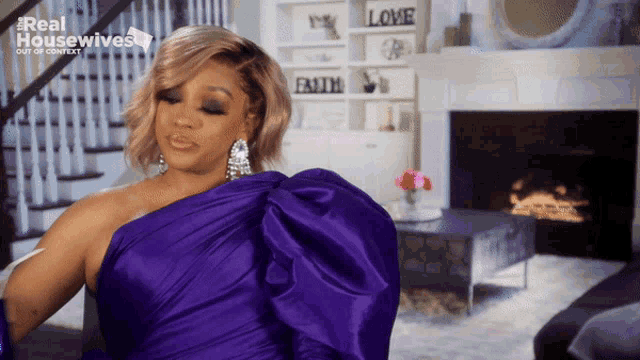 a woman in a purple dress is standing in front of a fireplace with the words real housewives on the bottom right