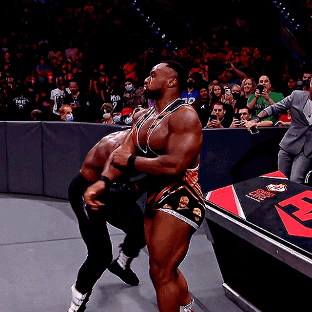 a wrestler holds another wrestler in a wrestling ring with the letter r on the floor
