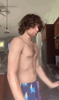 a shirtless man with curly hair is standing in a kitchen with his arms outstretched .